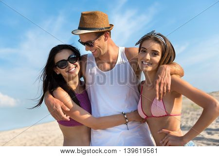 Glad to be with you. Cheerful handsome smiling man embracing attractive young women while resting on the beach
