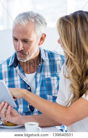 Woman showing digital tablet to man at table in restaurant