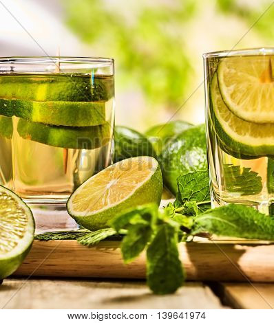 On wooden boards close up of two glasses with alcohol green transparent drink. Drink two hundred fifty five mojito cocktail with half lime and mint . Country life style. Light background.