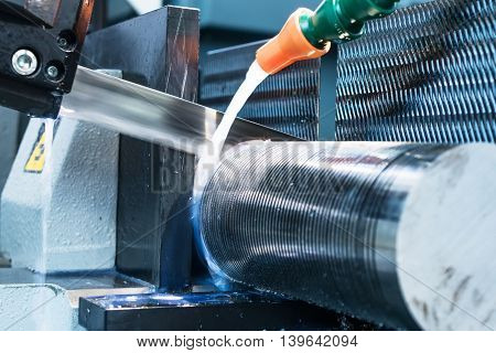 Automatic bandsaw sawing metal workpiece. From the cooling pipes supplied lubricity emulsion.