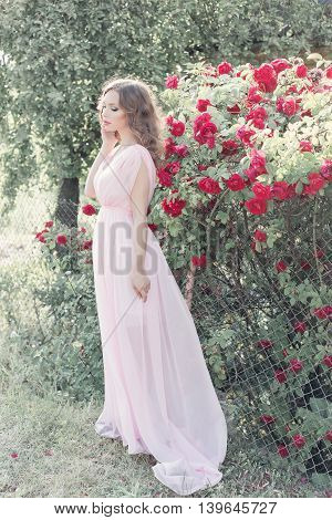 beautiful sexy girl in a light dress with delicate make-up and hair in a flower garden with roses in luchas sunlight at sunset. Styled photo fane art