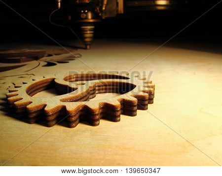 Plywood gear clipped by laser with a laser head and wood plate on a background