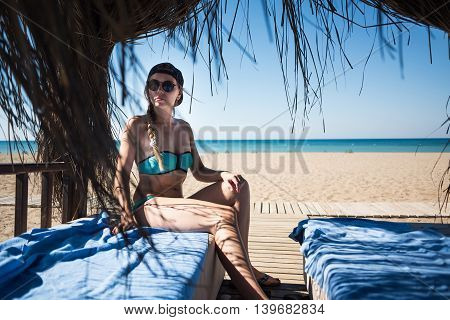 Beautiful young girl in bungalow with black sunglasses in blue swimsuit. View on the sea.