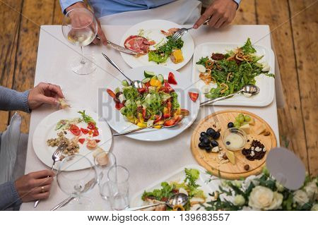People at the table eating a Greek salad, seafood and cheese plate.