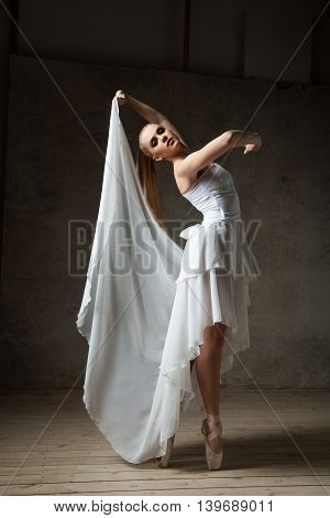 Portrait of attractive young blonde ballet dancer in white costume dancing in studio