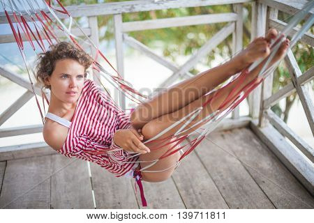 Photo young pretty girl relaxing on beach Bungalow in hammock. Smiling woman spending chill time outdoor summer. Caribbean Ocean Vacations. Horizontal, blurred background