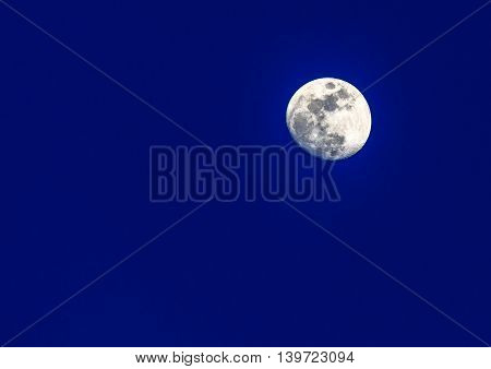 Full moon at sunrise in front of a blue sky.