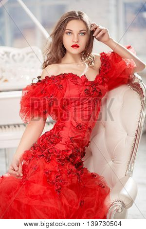 Beautiful woman in red dress sitting near the grand white piano.