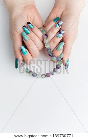 Closeup of woman nails with creative purple and green manicure. Fluorinit print. Natural stone beads. Copy space.