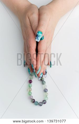 Closeup of woman nails with creative purple and green manicure. Fluorinit print. Natural stone beads. Copy space.
