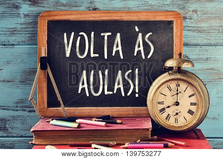 a chalkboard with the text volta as aulas, back to school in portuguese, some old books, an old clock, a compass and some pencil crayons of different colors, against a blue wooden background