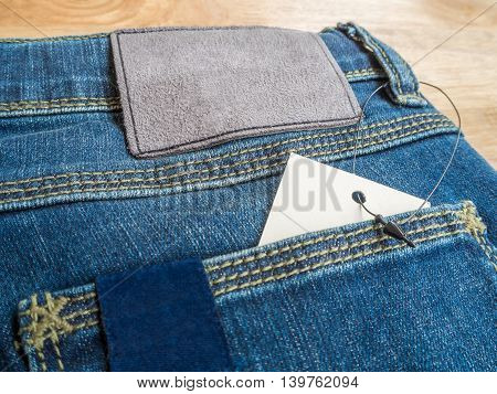 Close-up of blue jeans with deerskin label and white blank price tag in pocket on wooden texture background