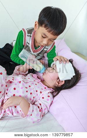 Sick sister lying and suck up milk on the bed kindly brother keep vigil over a sick of closely. Conceptual image about loving and bonding of sibling.