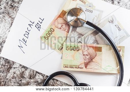 Stethoscope with wording of "Medical Bill" showing expensive healthcare or expensive medical bill with Indonesia Rupiah Bank Notes