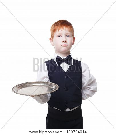 Little waiter stands with empty tray serving something. Redhead child boy in suit plays restaurant servant at blue background