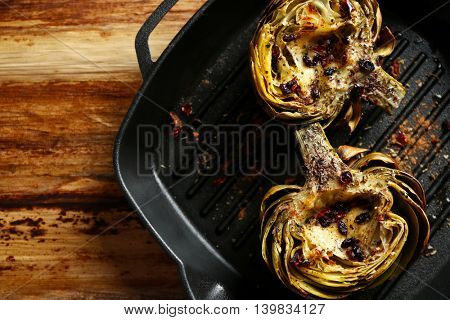 Baked artichokes in black grill pan on wooden background