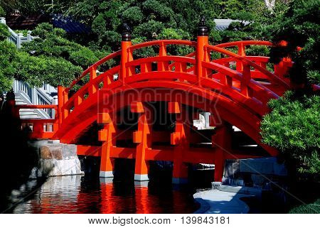 Hong Kong - January 1 2008: Classic bright orange Chinese wooden bridge spans a lagoon in the Nan Lian Garden