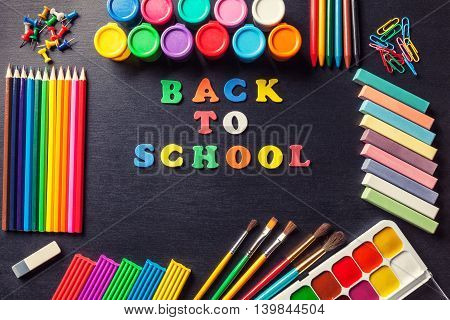 Colored letters frame laid out in the center of the phrase Back to school Various tools for painting and art in graphite black background. Accessories for drawing.