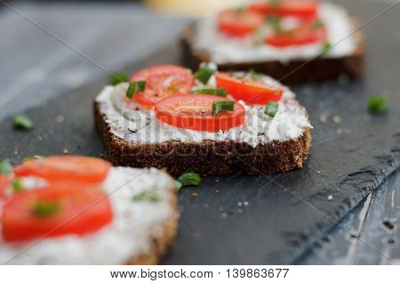 Bruschetta with feta cheese, fresh tomatoes and spices on a black rustic table