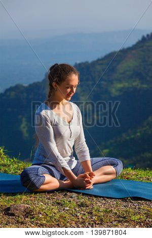 Sporty fit woman practices yoga asana Baddha Konasana - bound angle pose outdoors in HImalayas mountains in the morning with sky. Himachal Pradesh, India