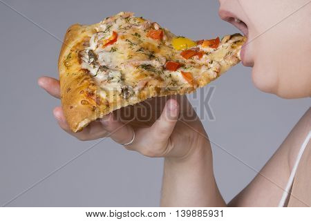 Fat woman with a piece of pizza in hand closeup on gray background obesity concept
