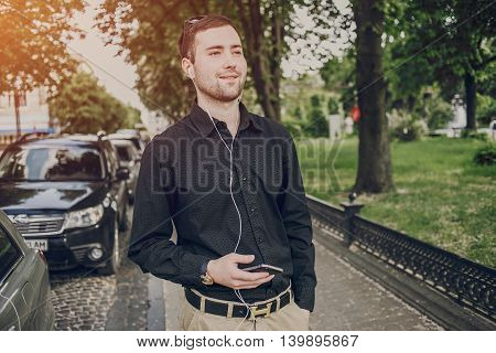 A guy in a nice town, walking, listening to music and taking pictures themselves on the phone