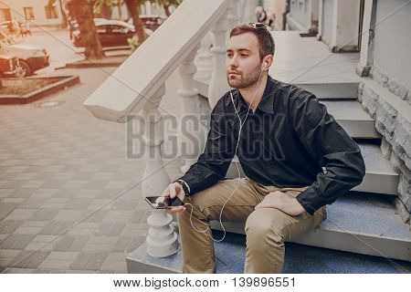 A guy in a nice town, walking, listening to music and taking pictures themselves on the phone