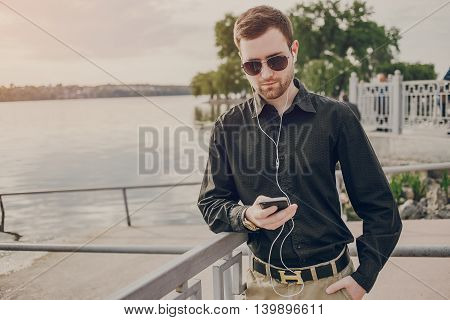 A guy in a nice town, walking, listening to music and taking pictures themselves on the phone