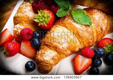 Fresh tasty croissants with berries on wooden background