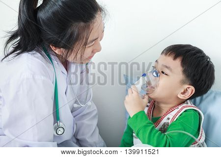 Happy child having respiratory illness helped by health professional with inhaler. Pediatrician take care asian boy with asthma problems making inhalation with mask on his face at hospital.