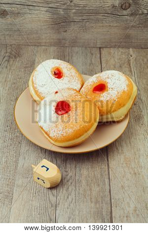Donut for jewish holiday hanukkah on plate and dreidel on wooden background
