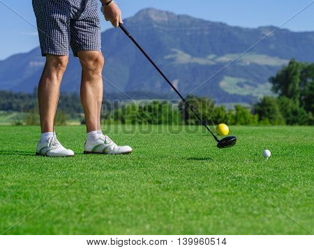 Photo of a male golfer teeing off on a golf course on a beautiful day.