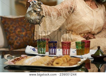 A Woman Pours Moroccan Tea From Traditional Moroccan Teapot Into Cups.