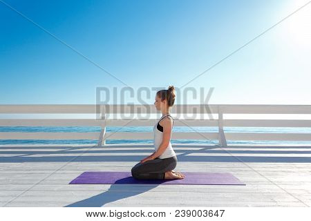 Young Slim Woman In Tight Sportswear Sitting On Purple Yoga Mat And Practicing Outdoors At White Woo