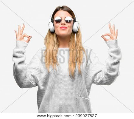 Young woman listen to music with headphone doing ok sign gesture with both hands expressing meditation and relaxation