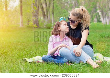 Mother And Daughter Resting On The Nature On The Green Grass, Resting, Smiling In The Summer In Sunn