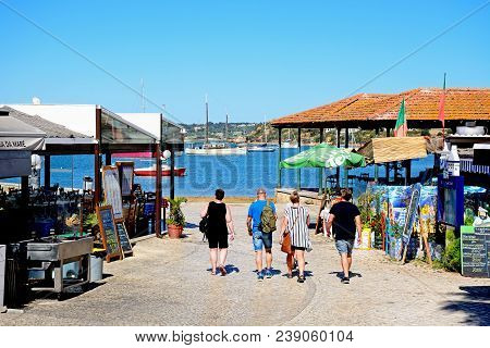 Alvor, Portugal - June 7, 2017 - Tourists Walking Along A Restaurant Lined Street With Views Towards