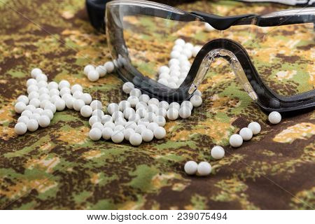 Balls Airsoft Bbs And Protective Glasses On A Camouflage Background