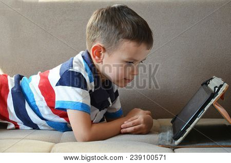 Little Cute Boy In T-shirt Playing Games On A Tablet And Watching Cartoons. Toddler With Tablet. At 