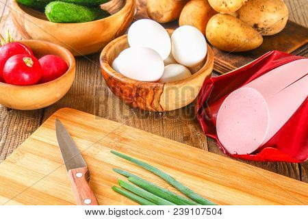 Ingredients For Okroshki - Sausage, Eggs, Radishes, Onions, Potatoes, Cucumbers On An Old Wooden Tab