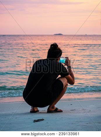 Asian Young Man Takes Pictures At The Beach With Sunset