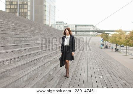 Businesswoman Standing On Stairs With Bag And High Buildings In Background. Concept Of Profession An