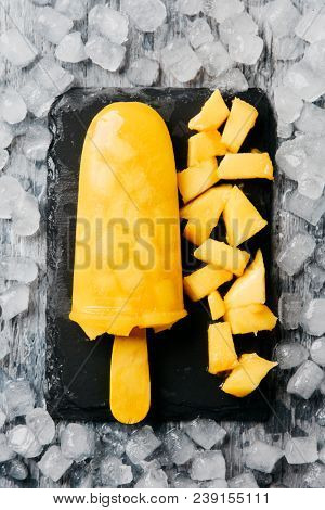 high angle view of a homemade ice pop, made with natural fruit juice and pieces of fruit, placed on a slate tray, on crushed ice