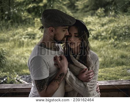Beautiful Young Couple Of Man And Woman In Summer Clothes Staying In Garden House Hugging On The Par