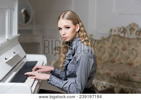 Young Victorian Girl In A Tender Blue Dress Learning To Play Piano. Lovely Blond With Curly Hair Wom