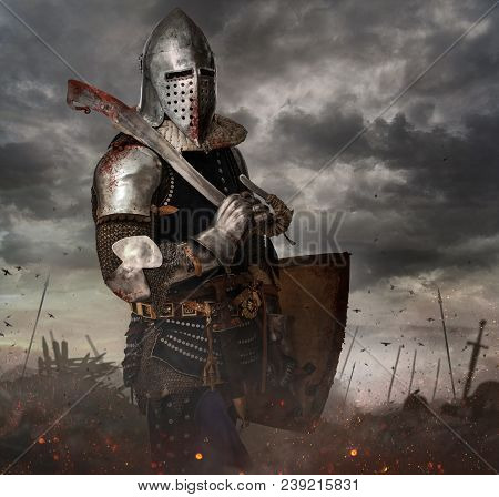 Knight With Sword In Battlefield With Dark Clouds On Background.