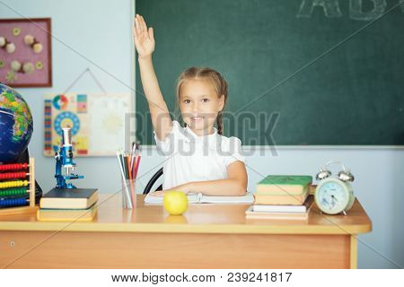 Cute Schoolgirl Pupil Raising Hand In Classroom.