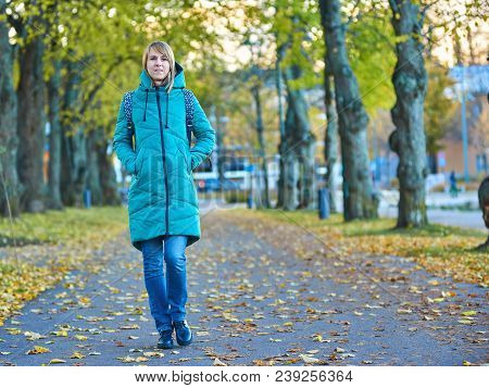 Young European Woman In A Green Coat Is Walking Around City Park In Autumn. She Is Strolling On The 