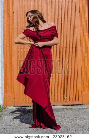Beautiful Young Woman In A Long Red Evening Gown With A Train Standing Next To The Old Door