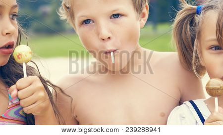 Cute Brother And Sisters Enjoying Their Lollipops Outside At The Beach.